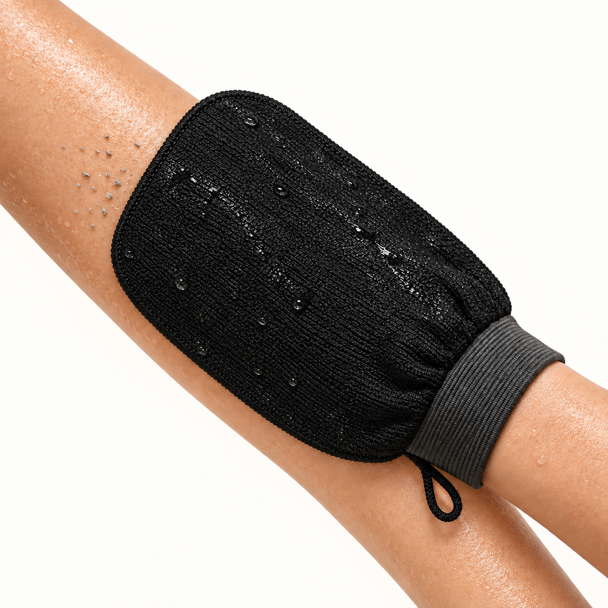 The wet glove mid-stroke on a forearm, lifted dead skin visible on the surface